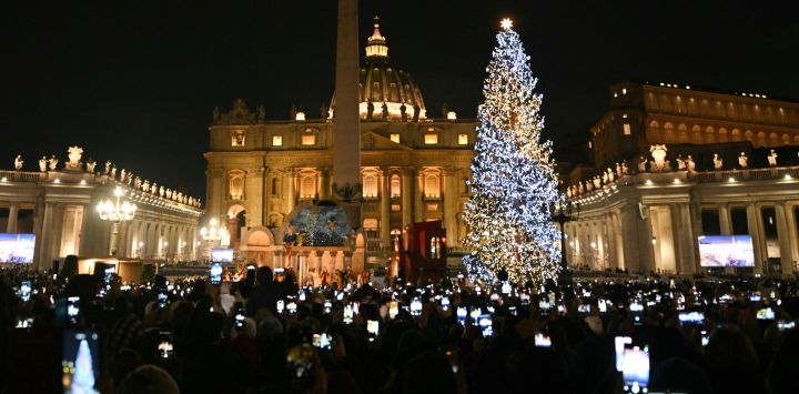 La gente toma fotos con sus teléfonos de la iluminación navideña en la Plaza de San Pedro, donde se inauguraron el árbol de Navidad y el belén en el Vaticano.
