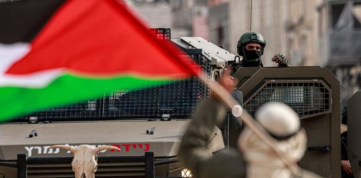 Un hombre palestino con su bandera nacional hace un gesto hacia un soldado israelí en el exterior del campo de refugiados palestinos de Nur Shams, en el norte de Cisjordania ocupado por Israel.