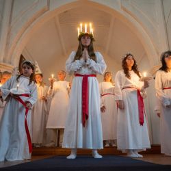 Florence Edwards (centro), interpretando a Lucía, se une al coro Lucía, compuesto por miembros de la Comunidad Nórdica Internacional de Liverpool, en el servicio sueco «Lucía: La Portadora de la Luz» en la iglesia Gustaf Adolfs Kyrka de Liverpool, noroeste de Inglaterra. En Suecia, Lucía es una de las tradiciones más significativas del calendario: Lucía conmemora a Lucía de Siracusa, una mártir de principios del siglo IV, que se dice que llevaba comida y ayuda a la gente con una corona de velas en la cabeza para tener las manos libres y poder llevar toda la comida que pudiera. | Foto:OLI SCARFF / AFP