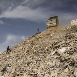 Trabajadores palestinos que participan en un proyecto de gestión de escombros, implementado y supervisado por el Programa de las Naciones Unidas para el Desarrollo (PNUD) para la Franja de Gaza, observan cómo los camiones trasladan hormigón, metal y escombros de edificios y casas destruidos durante la reapertura y gestión de las calles bloqueadas por los escombros en Khan Yunis, al sur de la Franja de Gaza, tras una tregua negociada por Estados Unidos que puso fin a dos años de guerra. | Foto:Bashar Taleb / AFP
