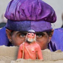 Un hombre observa desde detrás de una imagen de San Lázaro durante la peregrinación al Santuario de San Lázaro en El Rincón, cerca de La Habana, Cuba. Cada año en Cuba, los peregrinos rezan a San Lázaro por los católicos y a Babalú Ayé por las religiones afrocubanas, pidiendo salud, sanación y prosperidad en medio de la grave crisis económica que afecta a la isla. | Foto:YAMIL LAGE / AFP