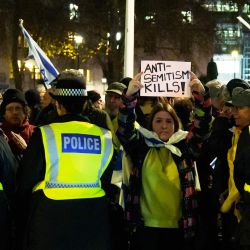 Una mujer sostiene un cartel que dice "El antisemitismo mata" entre agentes de policía mientras la gente participa en una ceremonia de encendido de velas de Janucá organizada por la Campaña contra el Antisemitismo y la organización judía Jabad Lubavitch en la Plaza del Parlamento, en el centro de Londres. | Foto:CARLOS JASSO / AFP