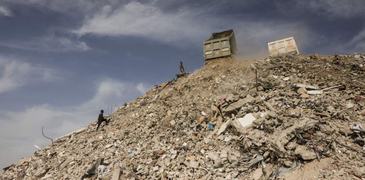 Trabajadores palestinos que participan en un proyecto de gestión de escombros, implementado y supervisado por el Programa de las Naciones Unidas para el Desarrollo (PNUD) para la Franja de Gaza, observan cómo los camiones trasladan hormigón, metal y escombros de edificios y casas destruidos durante la reapertura y gestión de las calles bloqueadas por los escombros en Khan Yunis, al sur de la Franja de Gaza, tras una tregua negociada por Estados Unidos que puso fin a dos años de guerra.