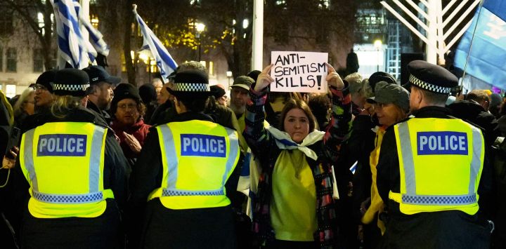 Una mujer sostiene un cartel que dice "El antisemitismo mata" entre agentes de policía mientras la gente participa en una ceremonia de encendido de velas de Janucá organizada por la Campaña contra el Antisemitismo y la organización judía Jabad Lubavitch en la Plaza del Parlamento, en el centro de Londres.