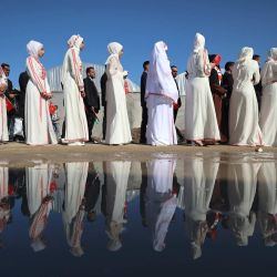 Novios hacen fila mientras unas 200 parejas se reúnen para una ceremonia nupcial multitudinaria bajo el lema "Amamos la vida a pesar del genocidio", organizada por la Fundación turca Al-Ribat en Al-Zawaida, en el centro de la Franja de Gaza. | Foto:Eyad Baba / AFP