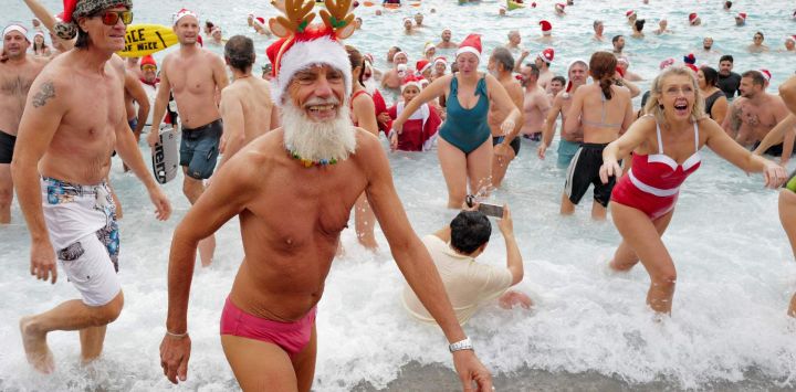 Bañistas vestidos de Papá Noel y otros con gorros navideños participan en el tradicional baño navideño en Niza, en la Riviera Francesa.
