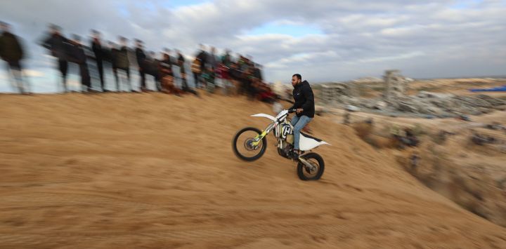 Palestinos desplazados observan a un motociclista recorrer las dunas de arena frente a los refugios para desplazados en el campamento de Nuseirat, en el centro de la Franja de Gaza.