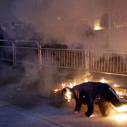 Un simpatizante de la oposición intenta extinguir el fuego que se le había caído encima tras ser atacado por error con un cóctel molotov durante una protesta frente a la oficina del Primer Ministro en Tirana. Los principales partidos de la oposición exigen la dimisión del gobierno tras las acusaciones contra Belinda Balluku, viceprimera ministra y ministra de Infraestructura y Energía de Albania. | Foto:Adnan Beci / AFP