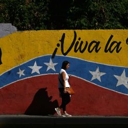 Una mujer pasa junto a un mural que representa al Libertador de Venezuela, Simón Bolívar, con la bandera nacional venezolana y la leyenda "¡Viva la patria!" en Caracas, dos días después de que el presidente venezolano, Nicolás Maduro, fuera capturado en un ataque estadounidense. | Foto:JUAN BARRETO / AFP