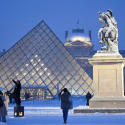 Un turista toma una foto de la pirámide del Louvre, diseñada por el arquitecto chino-estadounidense Ieoh Ming Pei, junto a la copia de la estatua "Louis XIV sous les traits de Marcus Curtius" de Bernin, cubierta de nieve en París. | Foto:Christophe Delattre / AFP