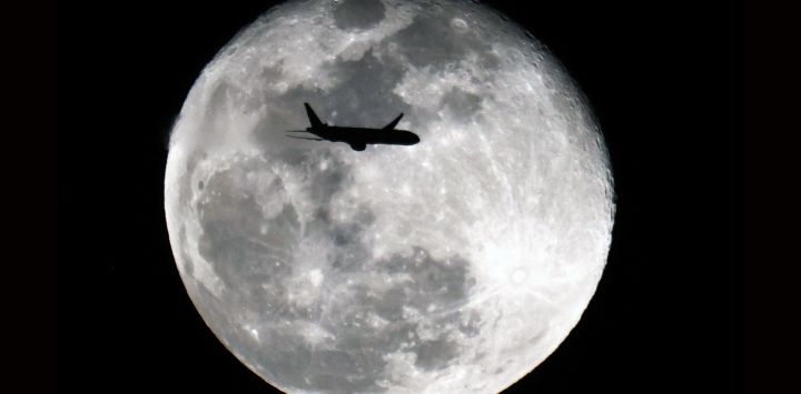 Un avión Boeing 777-369 (ER) de Kuwait Airways con destino a Bombay, India, se recorta contra la luna gibosa menguante sobre la ciudad de Kuwait.