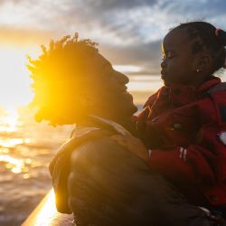 Un migrante juega con una niña pequeña a bordo del barco de rescate "Ocean Viking", operado por la ONG SOS Mediterranee, mientras navegan hacia el puerto de desembarque designado en Savona, noroeste de Italia. | Foto:SAMEER Al-DOUMY / AFP
