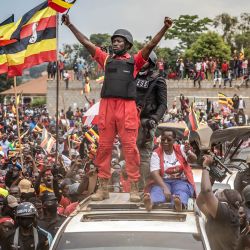 El líder de la oposición y candidato presidencial de la Plataforma de Unidad Nacional (PNU), Robert Kyagulanyi Ssentamu, conocido popularmente como Bobi Wine (centro), ondea una bandera ugandesa sobre un coche mientras es recibido por una multitud de simpatizantes durante un mitin de campaña en Mukono, antes de las elecciones generales ugandesas de 2026. | Foto:LUIS TATO / AFP