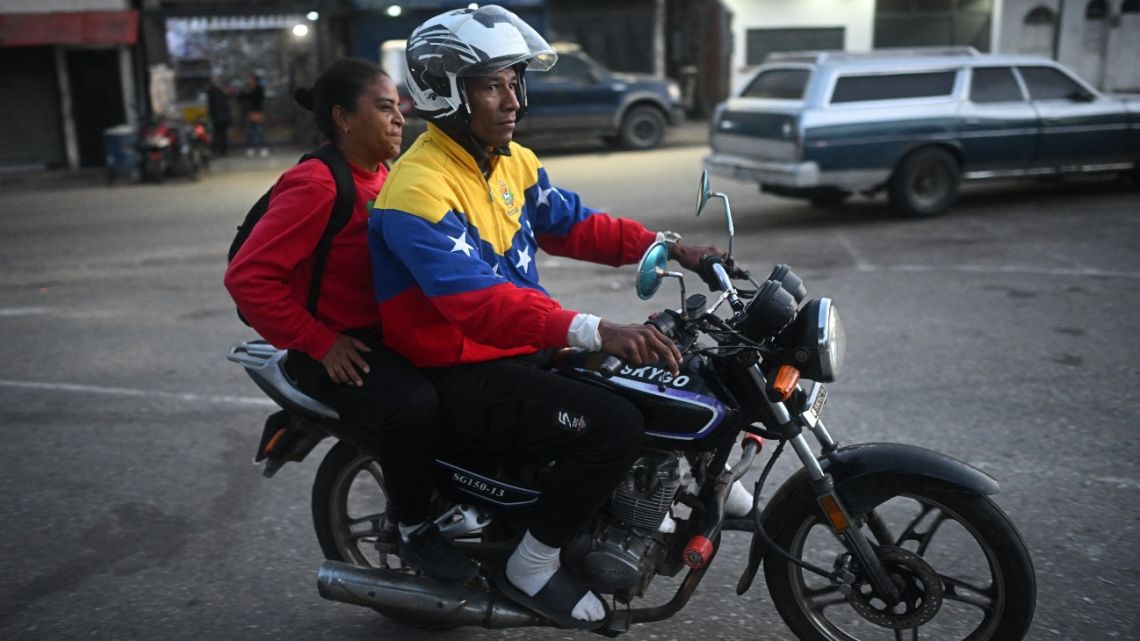 A moto taxi driver wearing a Venezuelan flag jacket drives a passenger in the surroundings of El Rodeo I prison in Guatire, Miranda State, some 30 kilometers east of Caracas on January 12, 2026. Venezuela said that 116 political prisoners have been…