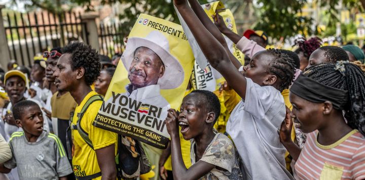 Jóvenes partidarios del actual presidente de Uganda y candidato presidencial del Movimiento de Resistencia Nacional (MRN), Yoweri Museveni, sostienen carteles electorales y corean consignas mientras hacen fila para ingresar al recinto de la manifestación antes del mitin de cierre de campaña del partido previo a las elecciones generales ugandesas.