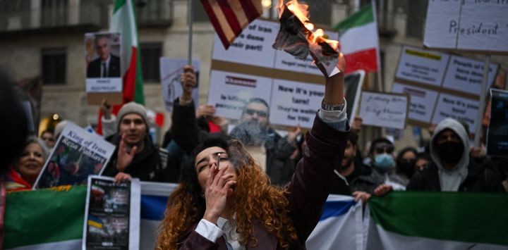 Un manifestante antirrégimen iraní enciende un cigarrillo con un papel encendido que representa a Ali Khamenei, líder supremo de Irán, durante una concentración frente al consulado estadounidense en Milán.