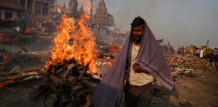 Un crematorio de la comunidad Dom pasa junto a las piras funerarias que arden en el Ghat Manikarnika, a orillas del río Ganges, en Varanasi, India.