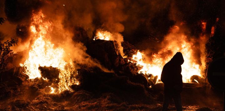 Un agricultor pasa junto a un incendio en una rotonda en Quimper, al oeste de Francia, durante un bloqueo agrícola para protestar contra el protocolo gubernamental de sacrificio obligatorio de ganado afectado por la dermatosis nodular contagiosa (DNC) y el acuerdo comercial entre la UE y el Mercosur.