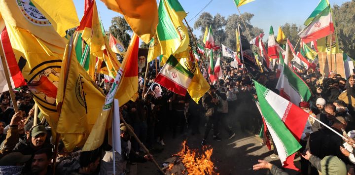 Manifestantes ondean banderas iraníes, junto con banderas de facciones armadas iraquíes leales a Irán, mientras queman banderas estadounidenses e israelíes durante una manifestación cerca de la embajada iraní en Bagdad, contra Israel y las recientes amenazas estadounidenses de acción militar en Irán, y en apoyo al régimen iraní y a su líder supremo.