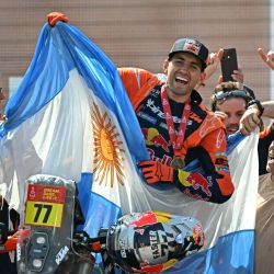 El piloto argentino Luciano Benavides con una Ktm 450 Rally Factory sostiene la bandera de su país mientras celebra en el podio tras ganar la 48ª edición del Rally Dakar 2026 en Yanbu, Arabia Saudita. | Foto:Giuseppe Cacace / AFP