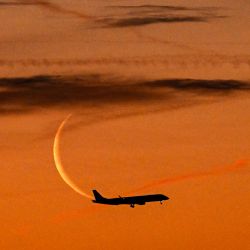Un avión sobrevuela la luna menguante antes del amanecer en Fráncfort del Meno, Alemania Occidental. | Foto:KIRILL KUDRYAVTSEV / AFP