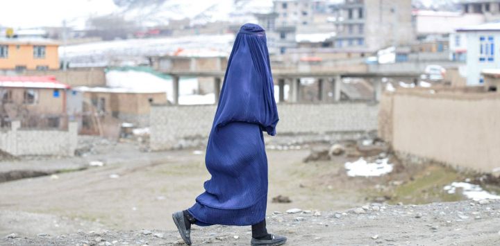 Una mujer afgana con burka camina por una calle con las montañas nevadas de fondo en el distrito de Argo, provincia de Badakhshan.