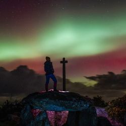 Un miembro del público observa la Aurora Boreal, o Luces del Norte, desde un dolmen, un megalito de 8000 años de antigüedad, después de una poderosa tormenta solar en Guilliguy, oeste de Francia. | Foto:Oscar Chuberre / AFP
