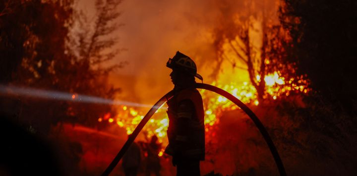Un bombero lleva una manguera mientras trabaja para extinguir la vegetación en llamas durante un incendio forestal en la localidad de Florida, cerca de la ciudad de Concepción, Chile.