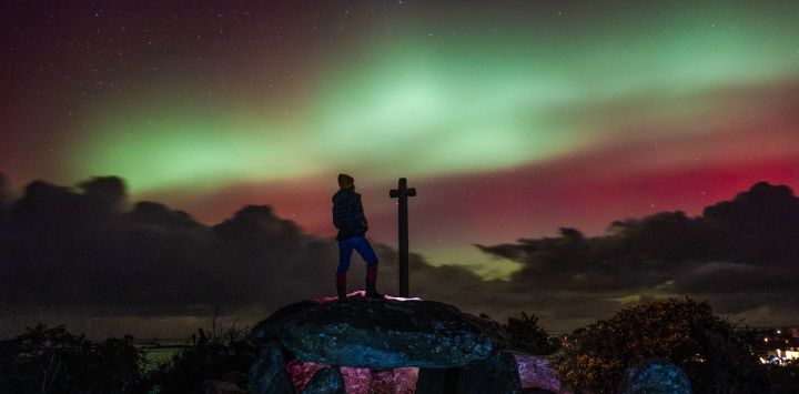 Un miembro del público observa la Aurora Boreal, o Luces del Norte, desde un dolmen, un megalito de 8000 años de antigüedad, después de una poderosa tormenta solar en Guilliguy, oeste de Francia.