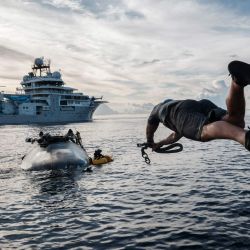 Esta foto muestra a la tripulación del OceanXplorer, un buque de investigación operado por la organización marina sin fines de lucro OceanX, saltando al mar desde un bote para nadar hacia un sumergible en la superficie y conectar una línea de recuperación en aguas cercanas a la isla de Sulawesi. Un sumergible con cúpula frontal se hunde bajo las olas frente a Indonesia, descendiendo casi 1000 metros hacia el reino de los corales de anillas púrpuras y los camarones bioluminiscentes. Este mes, AFP subió a bordo de uno de los dos sumergibles de OceanX, una organización fundada por el multimillonario Ray Dalio y su hijo, que trabaja con científicos en su barco OceanXplorer para estudiar el mundo marino. | Foto:Yasuyoshi Chiba / AFP