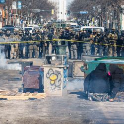 Manifestantes se refugian tras contenedores de basura volcados mientras una fila de agentes federales forma una barricada en una calle del centro durante los enfrentamientos tras el tiroteo mortal de un manifestante, en Minneapolis, Minnesota. | Foto:Kerem Yucel / AFP