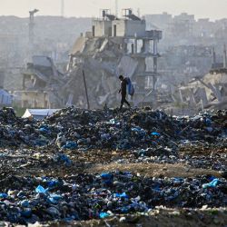 Un niño palestino busca material reciclable en un vertedero con el telón de fondo de edificios destruidos en Khan Yunis, al sur de la Franja de Gaza. Desde el 10 de octubre, una frágil tregua en Gaza, impulsada por Estados Unidos, ha frenado en gran medida los combates entre las fuerzas israelíes y Hamás, pero ambas partes han denunciado frecuentes violaciones. | Foto:Bashar Taleb / AFP