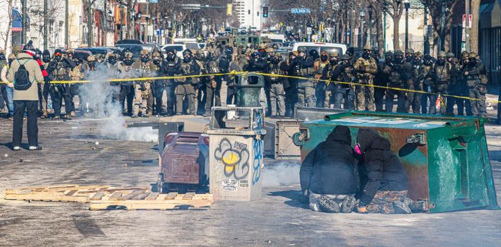 Manifestantes se refugian tras contenedores de basura volcados mientras una fila de agentes federales forma una barricada en una calle del centro durante los enfrentamientos tras el tiroteo mortal de un manifestante, en Minneapolis, Minnesota.