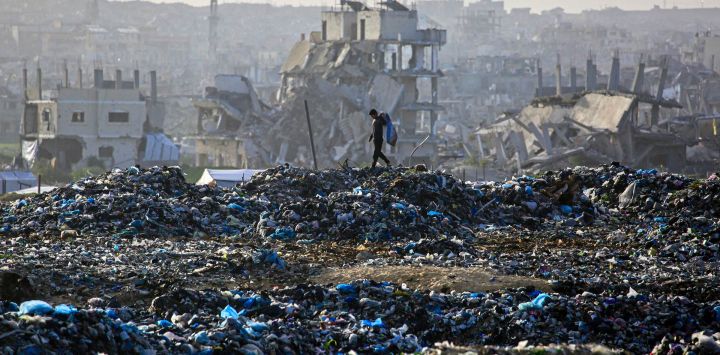Un niño palestino busca material reciclable en un vertedero con el telón de fondo de edificios destruidos en Khan Yunis, al sur de la Franja de Gaza. Desde el 10 de octubre, una frágil tregua en Gaza, impulsada por Estados Unidos, ha frenado en gran medida los combates entre las fuerzas israelíes y Hamás, pero ambas partes han denunciado frecuentes violaciones.