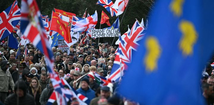 Una marcha de manifestantes ondeando banderas se aleja de la entrada del Campo de Entrenamiento de Crowborough, un antiguo emplazamiento militar, en Crowborough, sureste de Inglaterra, durante una protesta para exigir que los barracones no se utilicen para albergar a solicitantes de asilo. El gobierno británico confirmó que los primeros 27 inmigrantes ilegales habían sido trasladados al cuartel militar de Crowborough, en East Sussex, que albergará a más de 500 inmigrantes ilegales.