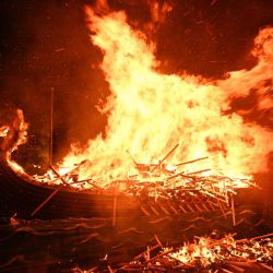 La gente observa el ardor del drakkar vikingo Up Helly Aa "Jarl Squad" en Lerwick, Islas Shetland, durante el festival Up Helly Aa. Up Helly Aa celebra la influencia de los vikingos escandinavos en las Islas Shetland y culmina con hasta 1000 "guizers" (hombres disfrazados) lanzando antorchas encendidas a su drakkar vikingo y prendiéndole fuego al anochecer. | Foto:Andy Buchanan / AFP