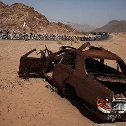 El grupo pasa junto a un coche abandonado durante la tercera etapa del AlUla Tour, de 142,1 km entre Winter Park y Bir Jaydah Mountain Wirkah. | Foto:ANNE-CHRISTINE POUJOULAT / AFP