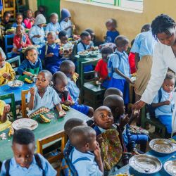 Imagen de una maestra ayudando a niños a comer su almuerzo en un salón de clase de una escuela, en el distrito de Bugesera, en la provincia Oriental, en Ruanda. Bajo un programa de apoyo infantil lanzado en 2023, los niños aquí reciben alimentos en escuelas para atender sus problemas de nutrición. | Foto:Xinhua/Cyril Ndegeya)