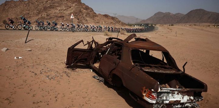 El grupo pasa junto a un coche abandonado durante la tercera etapa del AlUla Tour, de 142,1 km entre Winter Park y Bir Jaydah Mountain Wirkah.