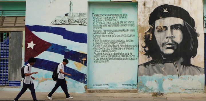 Imagen de dos jóvenes caminando frente a un muro pintado con el retrato del Che Guevara, en La Habana, Cuba.