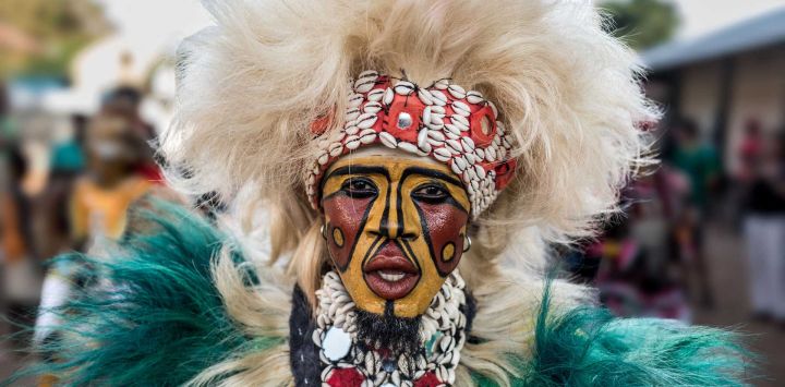 Un hombre con una máscara tradicional de simba, un famoso atuendo senegalés hecho con telas artesanales, danza por las calles durante el Festival Janjanbureh Kankurang en Janjanbureh, Región Central del Río. Este festival es una expresión del patrimonio cultural mandinga, celebrando la identidad, los valores comunitarios y la continuidad de la tradición. El Festival Janjanbureh Kankurang se ha convertido en un evento cultural de varios días que reúne a portadores de la cultura, artistas, intérpretes y visitantes de toda Gambia y el extranjero.