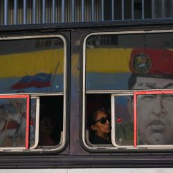 Una mujer viaja en un autobús mientras se ve el reflejo de un mural que representa al fallecido presidente venezolano Hugo Chávez en una ventana en Caracas. | Foto:Federico Parra / AFP