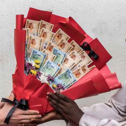 Una mujer reacciona al recibir un ramo hecho de billetes y flores de su novio como sorpresa antes del Día de San Valentín durante un encuentro en Kampala. Foto de Badru Katumba / AFP | Foto:AFP
