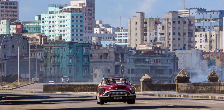 Turistas viajan en un antiguo coche estadounidense usado como taxi por una tranquila avenida en La Habana. Foto de ADALBERTO ROQUE / AFP
