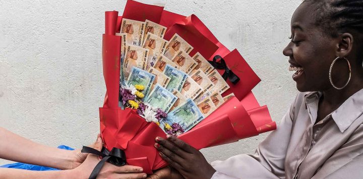 Una mujer reacciona al recibir un ramo hecho de billetes y flores de su novio como sorpresa antes del Día de San Valentín durante un encuentro en Kampala. Foto de Badru Katumba / AFP