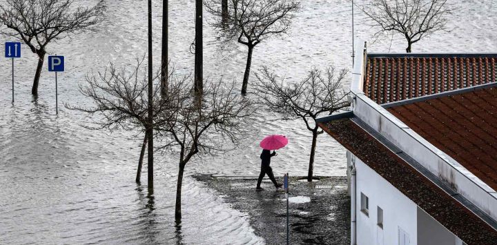 Un hombre sosteniendo un paraguas camina por una calle inundada en el pueblo de Montemor-o-Velho, Coimbra. Portugal. Foto de PATRICIA DE MELO MOREIRA / AFP