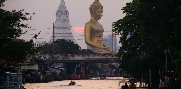 La gente navega en botes por un canal mientras el sol se pone detrás de la estatua gigante de Buda en Bangkok. Foto de Anthony WALLACE / AFP