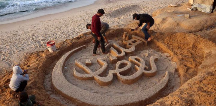 Yazeed Abu Jarad, quien fue desplazado por la guerra de Beit Lahia en el norte de la Franja de Gaza, crea una escultura de arena con el mensaje de saludo "Bienvenido, Ramadán". Foto de Bashar Taleb / AFP