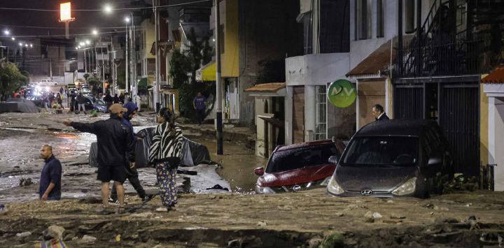 Personas observan junto a autos y casas afectadas por fuertes lluvias en el distrito de Yanahuara, en Arequipa, sur de Perú. Foto de Juan Santy / AFP