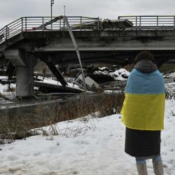 Una mujer envuelta en la bandera ucraniana se encuentra frente a un puente destruido en Irpin, al noroeste de Kyiv, durante una ceremonia conmemorativa. Foto de Genya SAVILOV / AFP | Foto:AFP